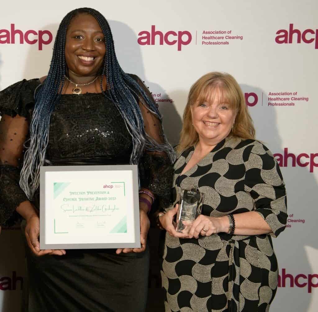 Zalika and Sue smiling for a picture, holding a certificate and award. 