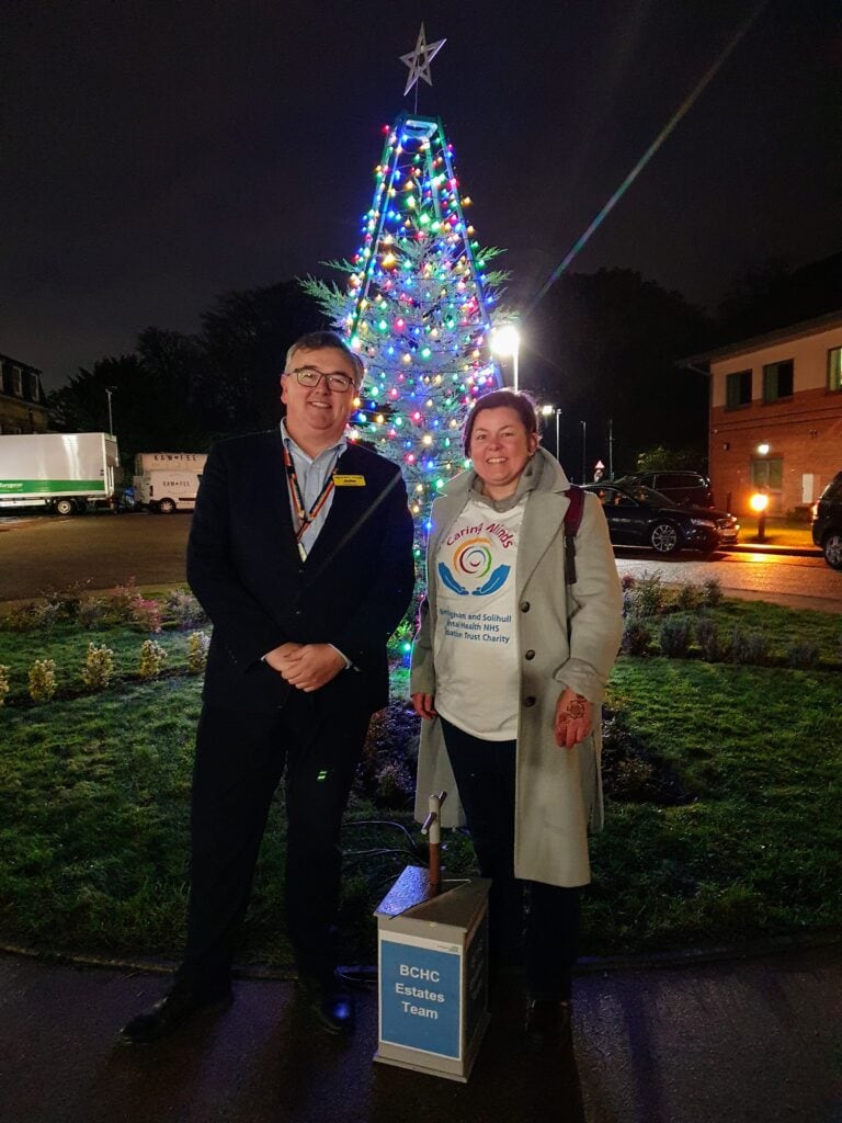 John Travers and Hele Tomblin smiling in front of a lit tree 