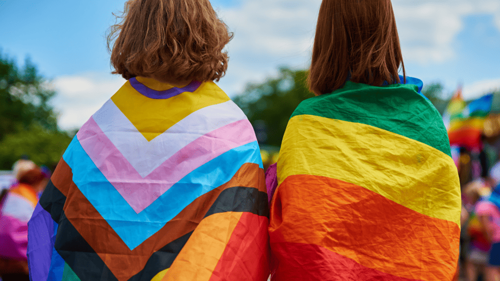 two people with an lgbtq+ flag draped over their shoulders